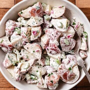 Creamy red potato salad with celery, red onion, fresh dill, and black pepper in a white serving bowl.