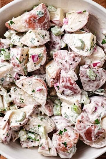 Creamy red potato salad with celery, red onion, fresh dill, and black pepper in a white serving bowl.