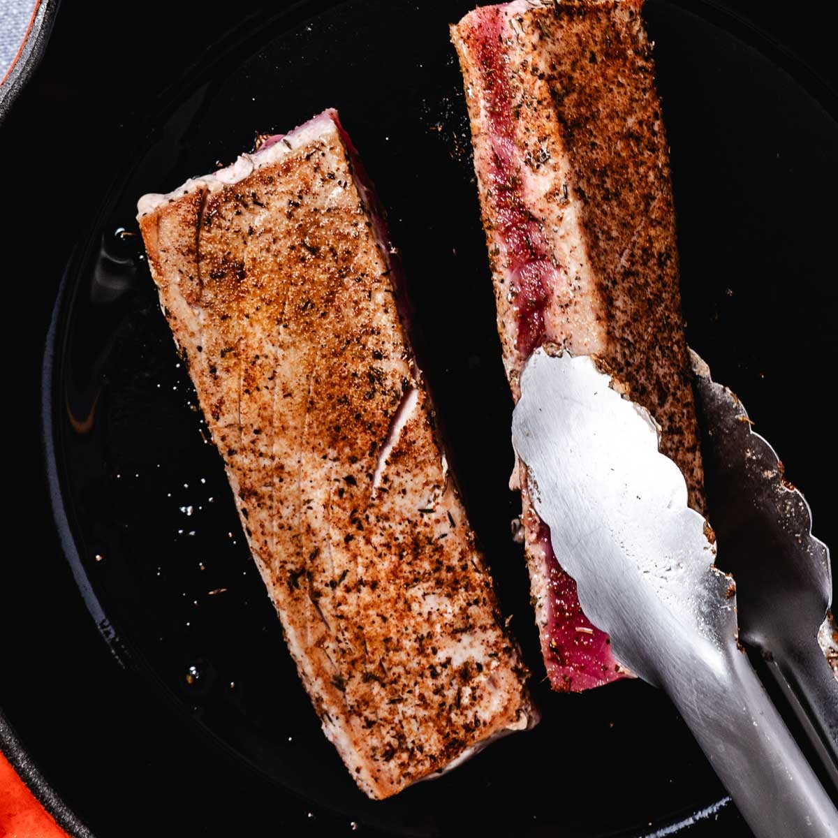 Blackened ahi tuna steaks searing in a hot cast-iron skillet