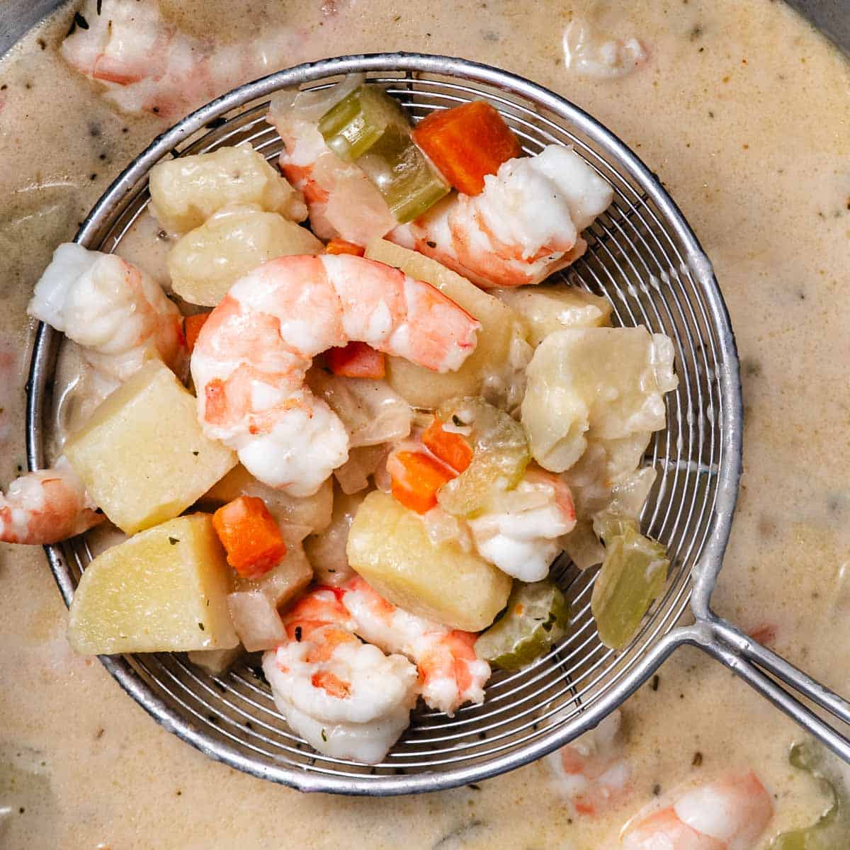 pot of shrimp chowder showing shrimp, potatoes, carrots and celery lifted out of pot.