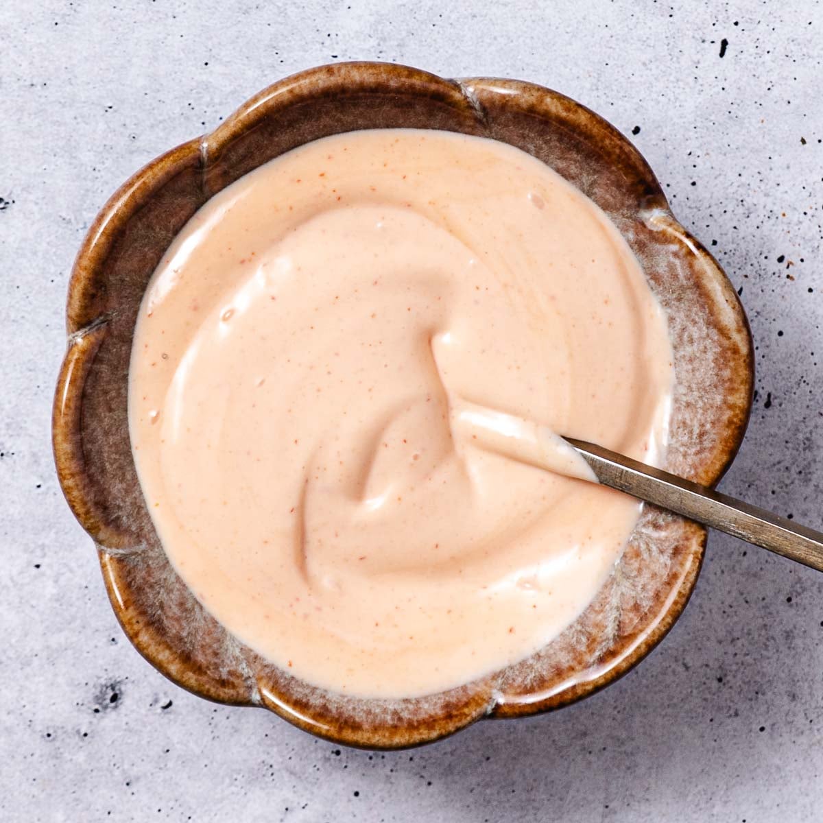 Homemade spicy mayo in a brown flower-shaped bowl with a spoon