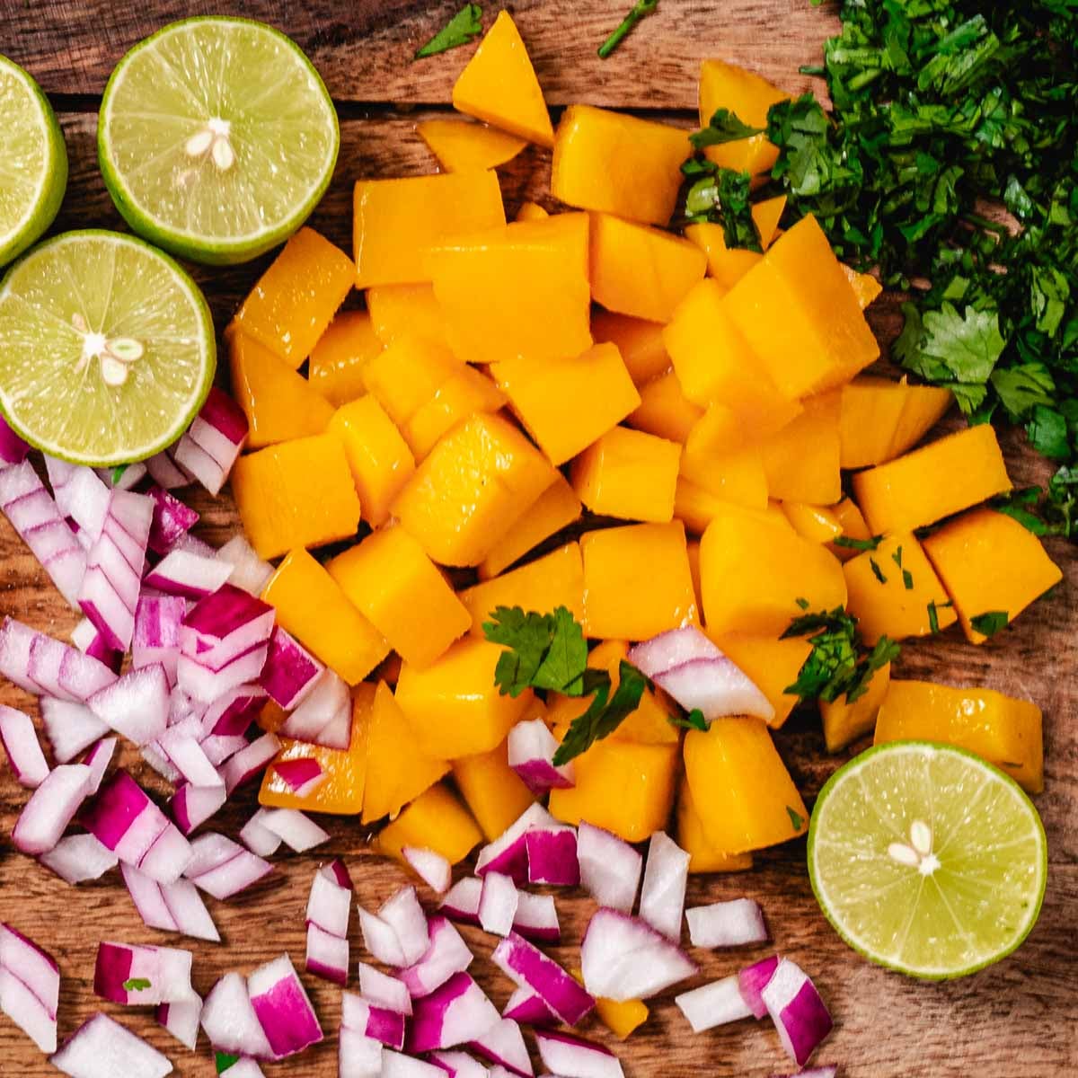Mango salsa ingredients with diced mango, red onion, cilantro, and fresh limes on a wood board