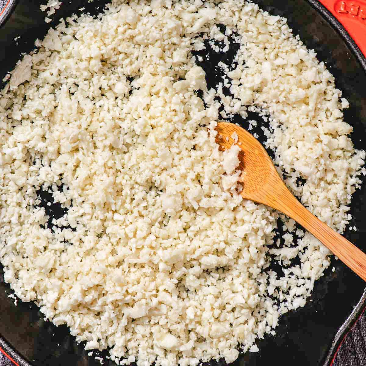 cooking cauliflower rice in skillet with wooden spoon