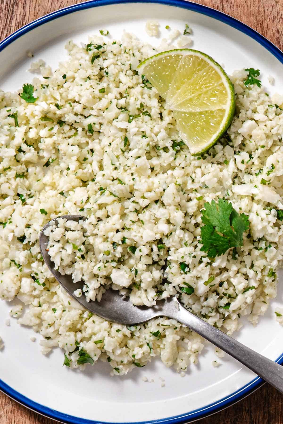 Cilantro lime cauliflower rice served on a white plate with a fresh lime wedge and a spoon ready to serve.