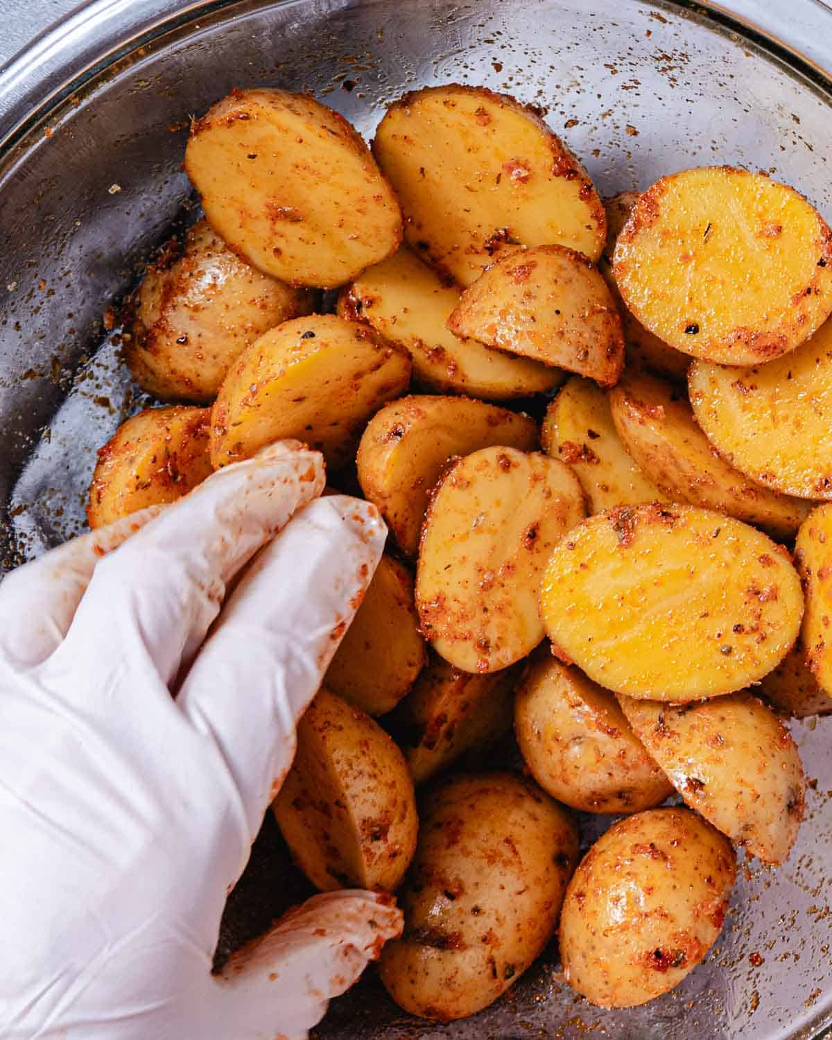 Gloved hand tossing baby potatoes with olive oil and seasonings