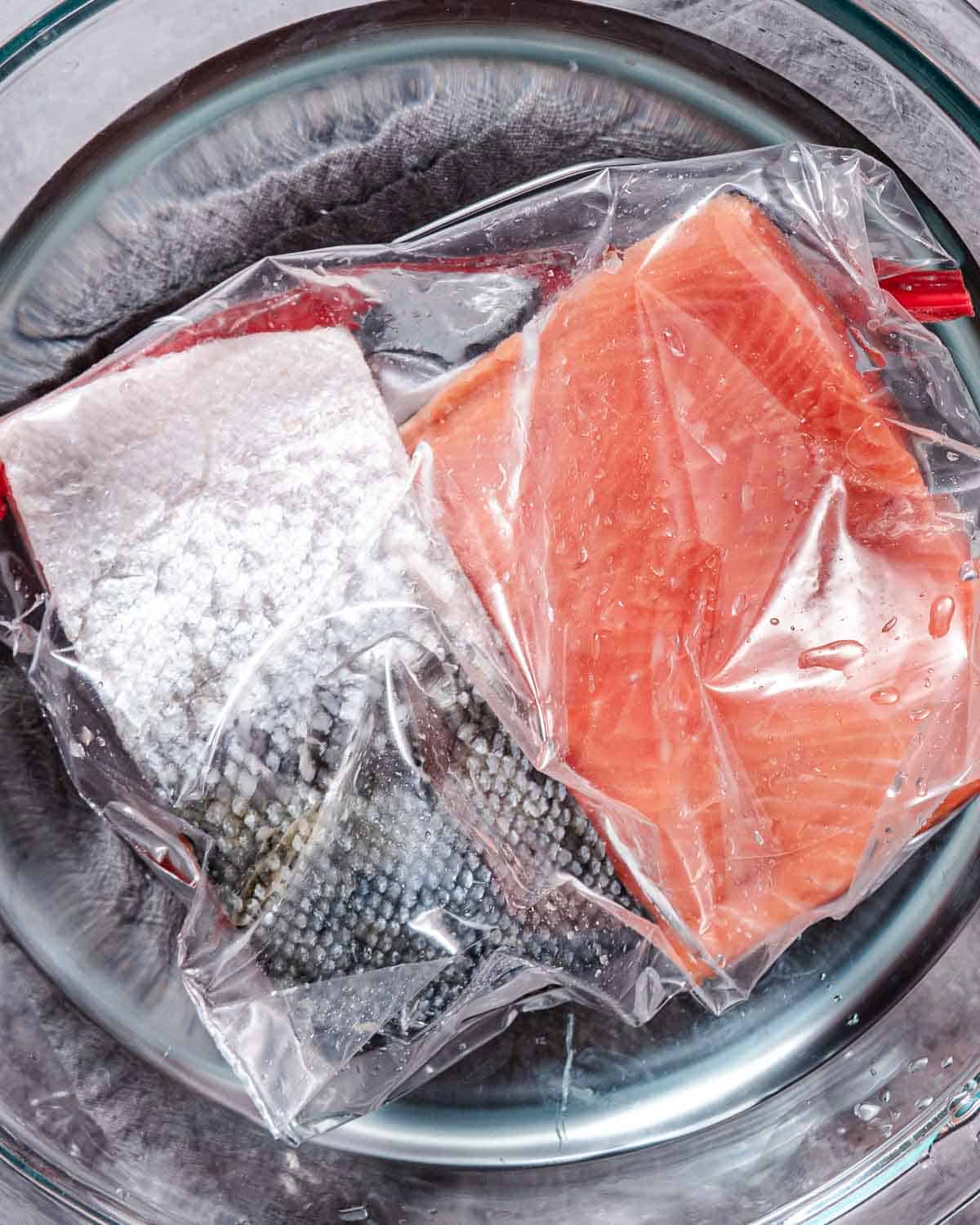 Frozen salmon fillets defrosting in a bowl of cold water.