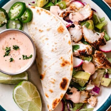 Blackened fish taco salad with avocado, jalapeños, radishes, lime, flour tortillas, and creamy taco sauce.