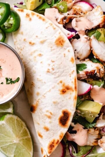 Blackened fish taco salad with avocado, jalapeños, radishes, lime, flour tortillas, and creamy taco sauce.