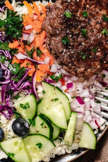Veggie burger bowl with cauliflower rice, carrots, cabbage, cucumbers, red onions, parsley, and fresh blueberries.