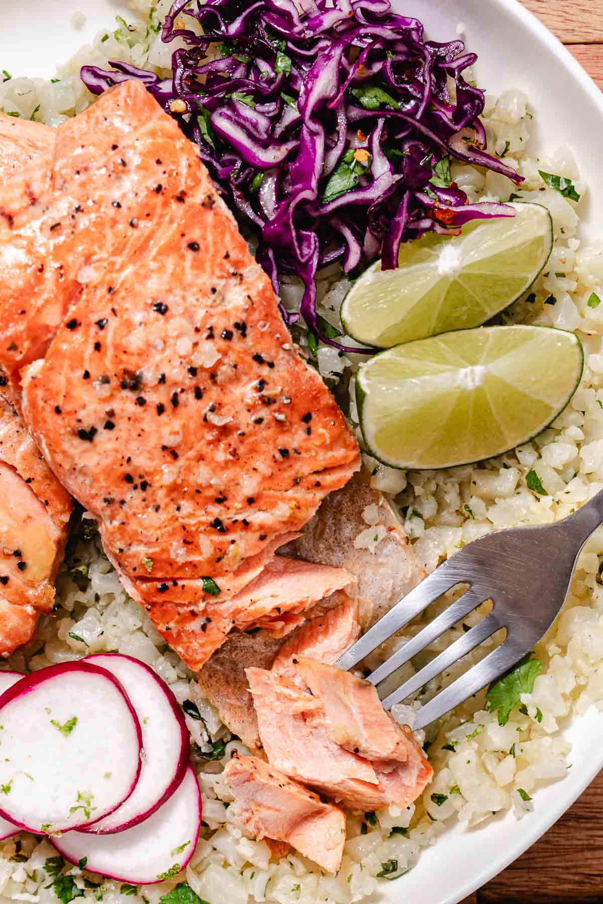 Cilantro lime cauliflower rice served with seared salmon, red cabbage slaw, radishes, and lime wedges.