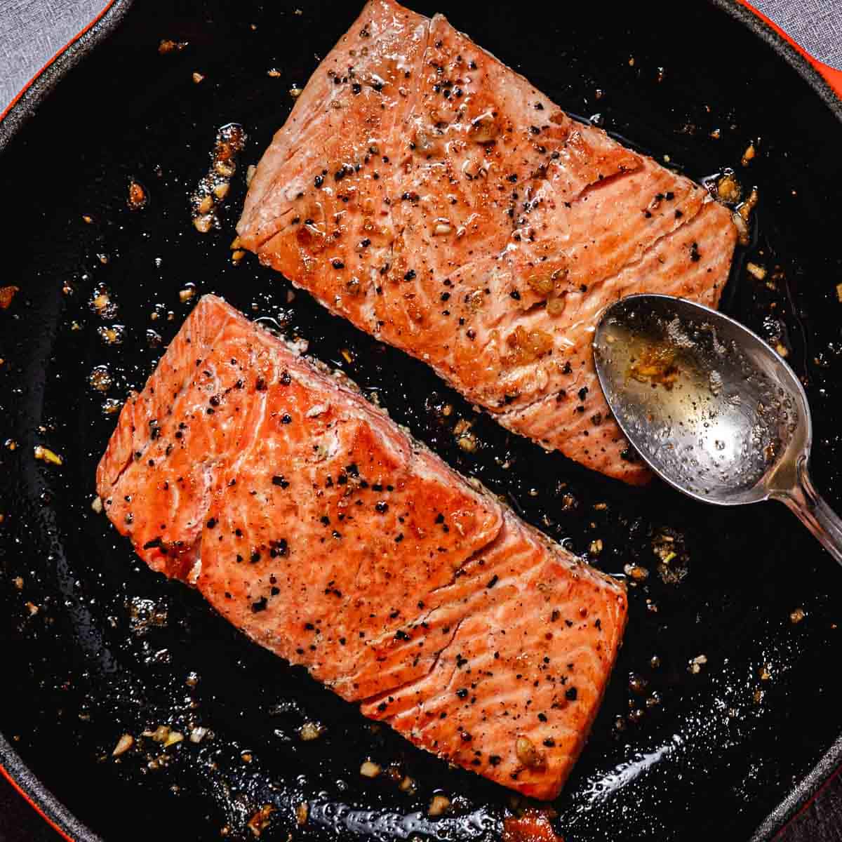 Pan seared coho salmon fillets basted with garlic butter in a skillet.