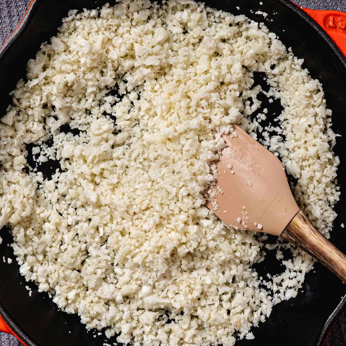 Fresh cauliflower rice cooking in butter and kosher salt in a skillet before adding lime juice and chopped cilantro.