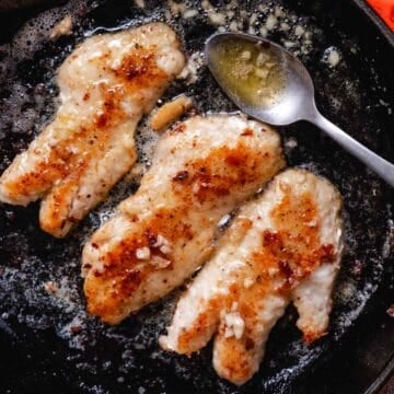Blackbelly rosefish fillets cooking in garlic butter in a cast-iron skillet