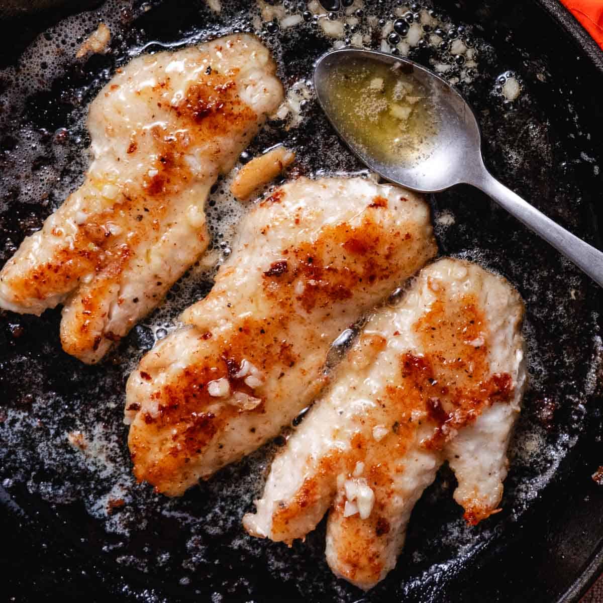 Blackbelly rosefish fillets cooking in garlic butter in a cast-iron skillet