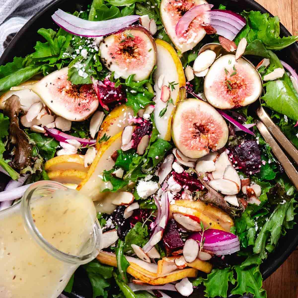 Lemon Dijon dressing poured over beet and pear salad with figs, feta, almonds, red onion, and mixed greens.