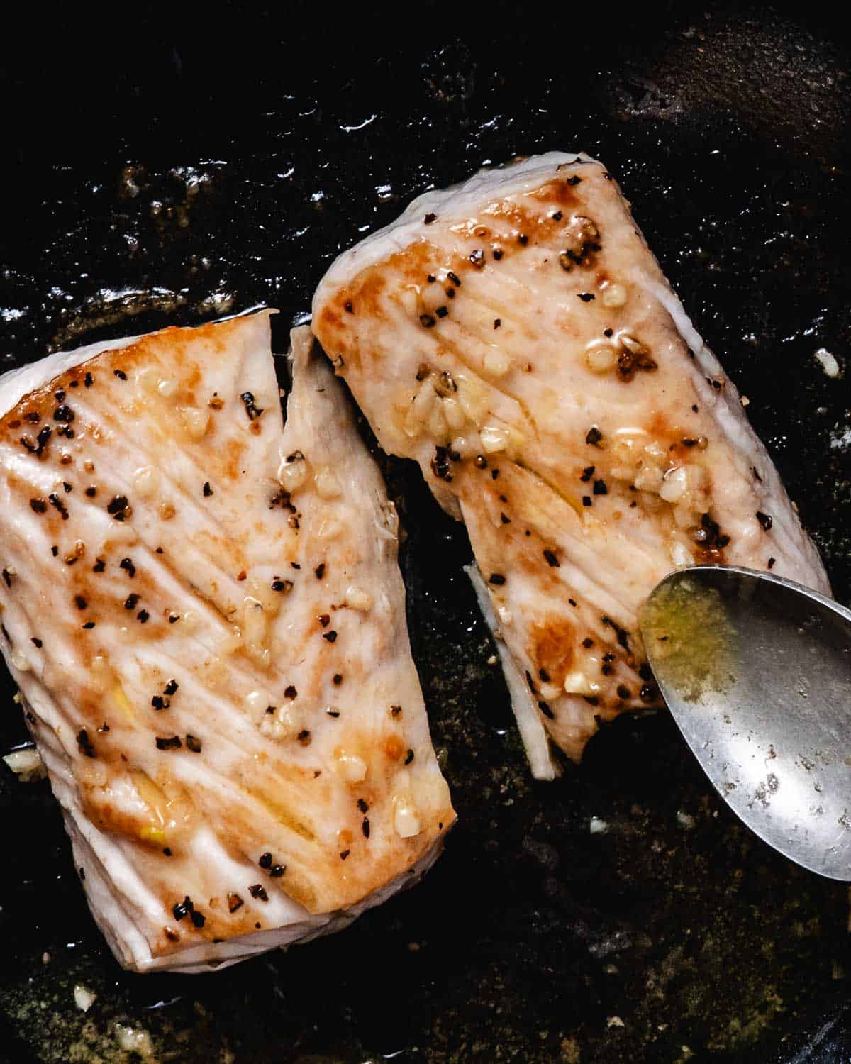 Pan-seared fresh mahi mahi fillets basted with garlic butter in a black skillet.