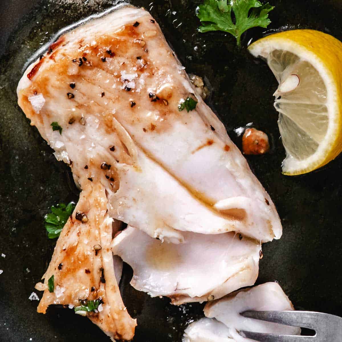 Cooked fresh mahi mahi opened to show the moist white center with lemon and parsley in a skillet.
