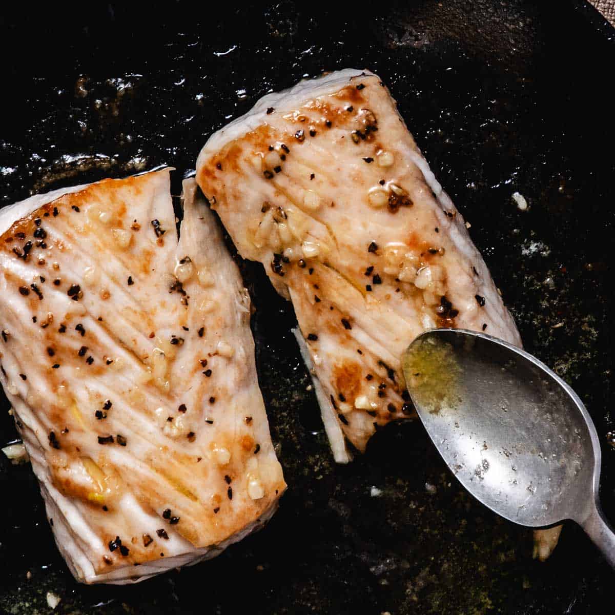 Pan-seared fresh mahi mahi fillets basted with garlic butter in a black skillet.