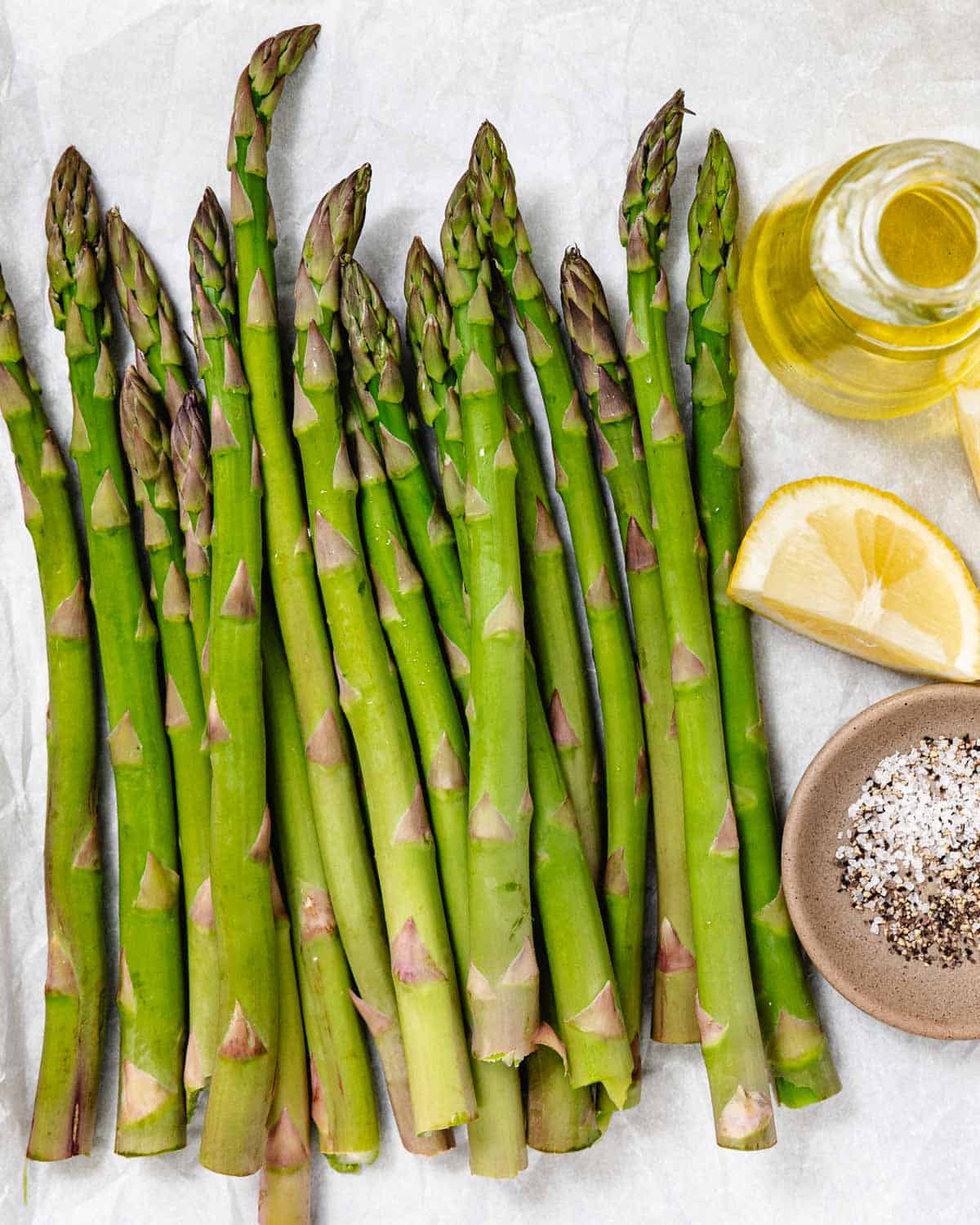 Ingredients for grilled asparagus are trimmed asparagus with olive oil, lemon, salt, and pepper.