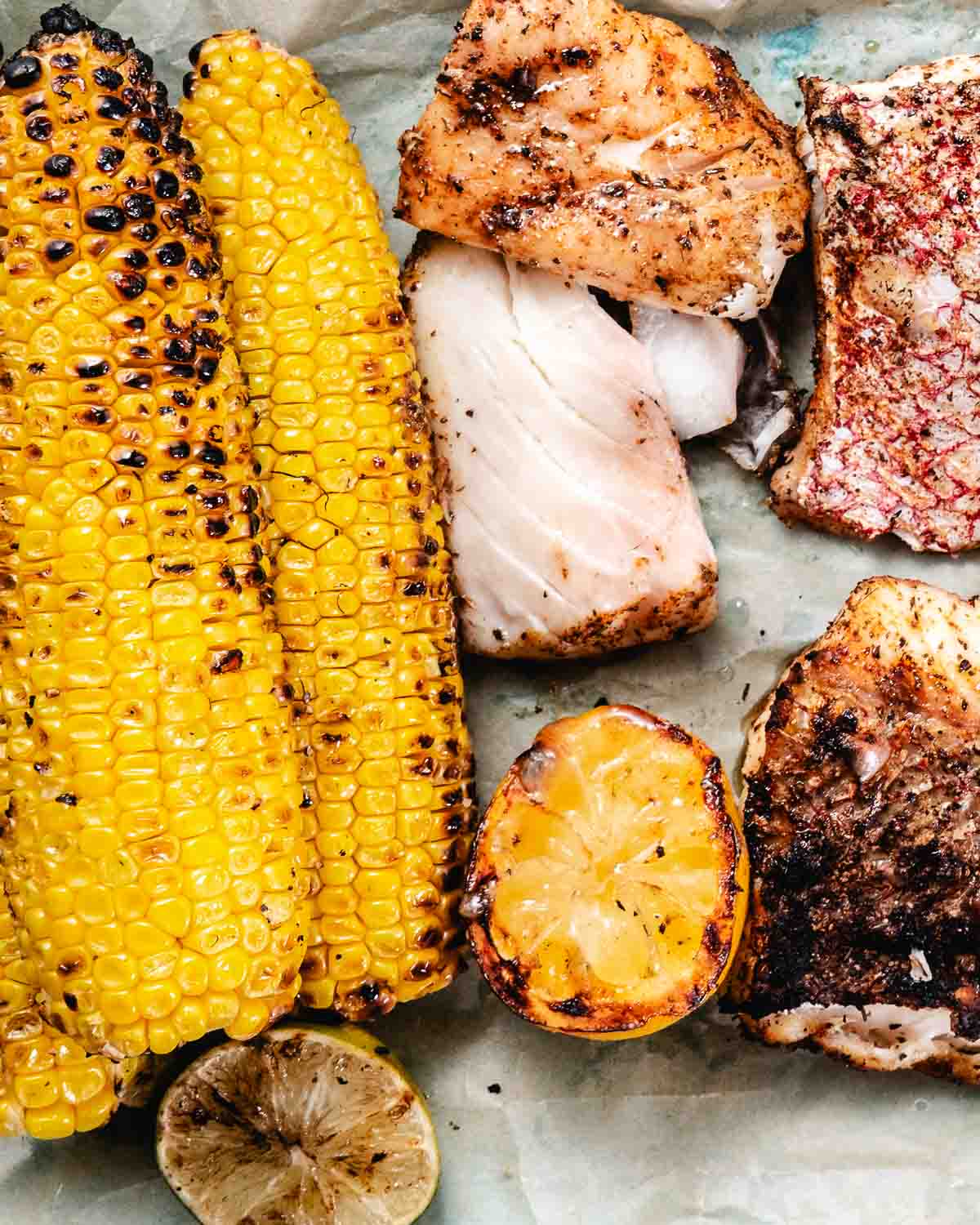 Grilled fish and corn on the cob with grilled lime halves.