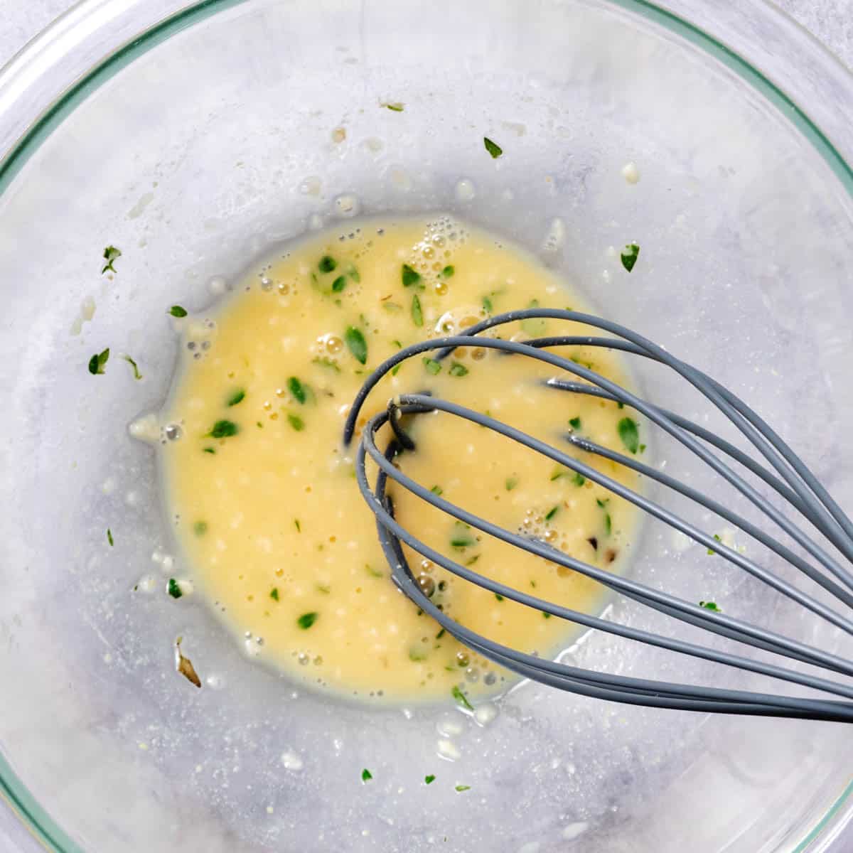 whisking lemon dijon vinaigrette in a glass bowl.