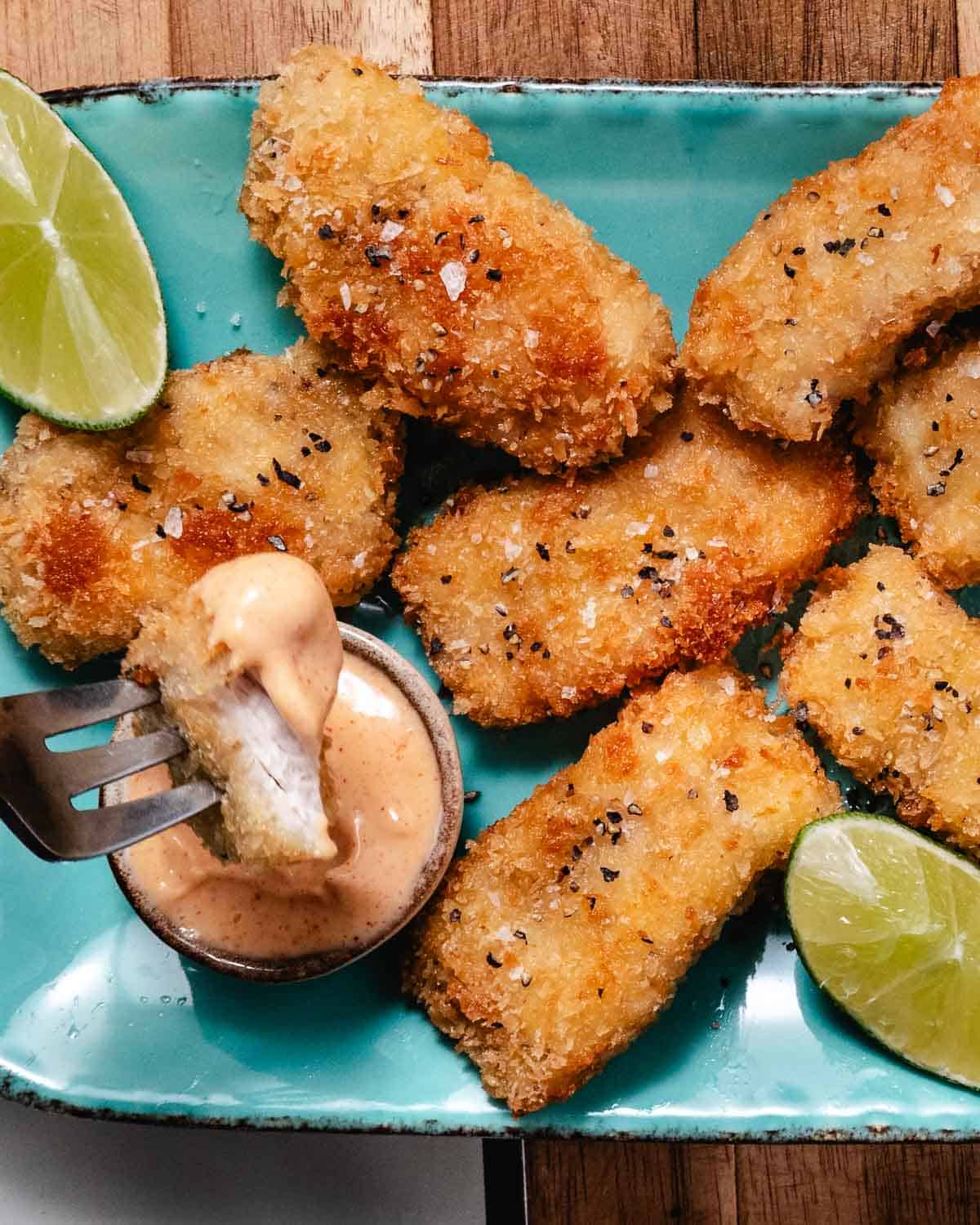 Fried mahi mahi bite dipped in creamy pink sauce with lime wedges.
