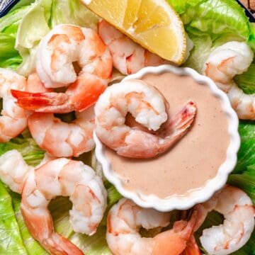 Bowl of Marie Rose sauce surrounded by cooked shrimp over iceberg lettuce and a lemon wedge.