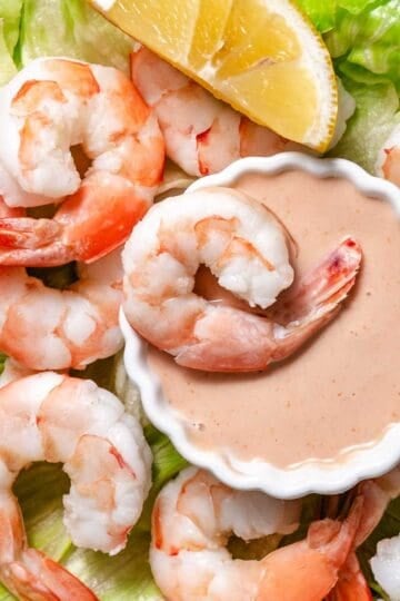 Bowl of Marie Rose sauce surrounded by cooked shrimp over iceberg lettuce and a lemon wedge.