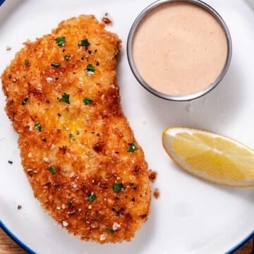 Crispy pan-fried halibut with lemon and creamy dipping sauce on a white plate