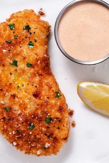 Crispy pan-fried halibut with lemon and creamy dipping sauce on a white plate
