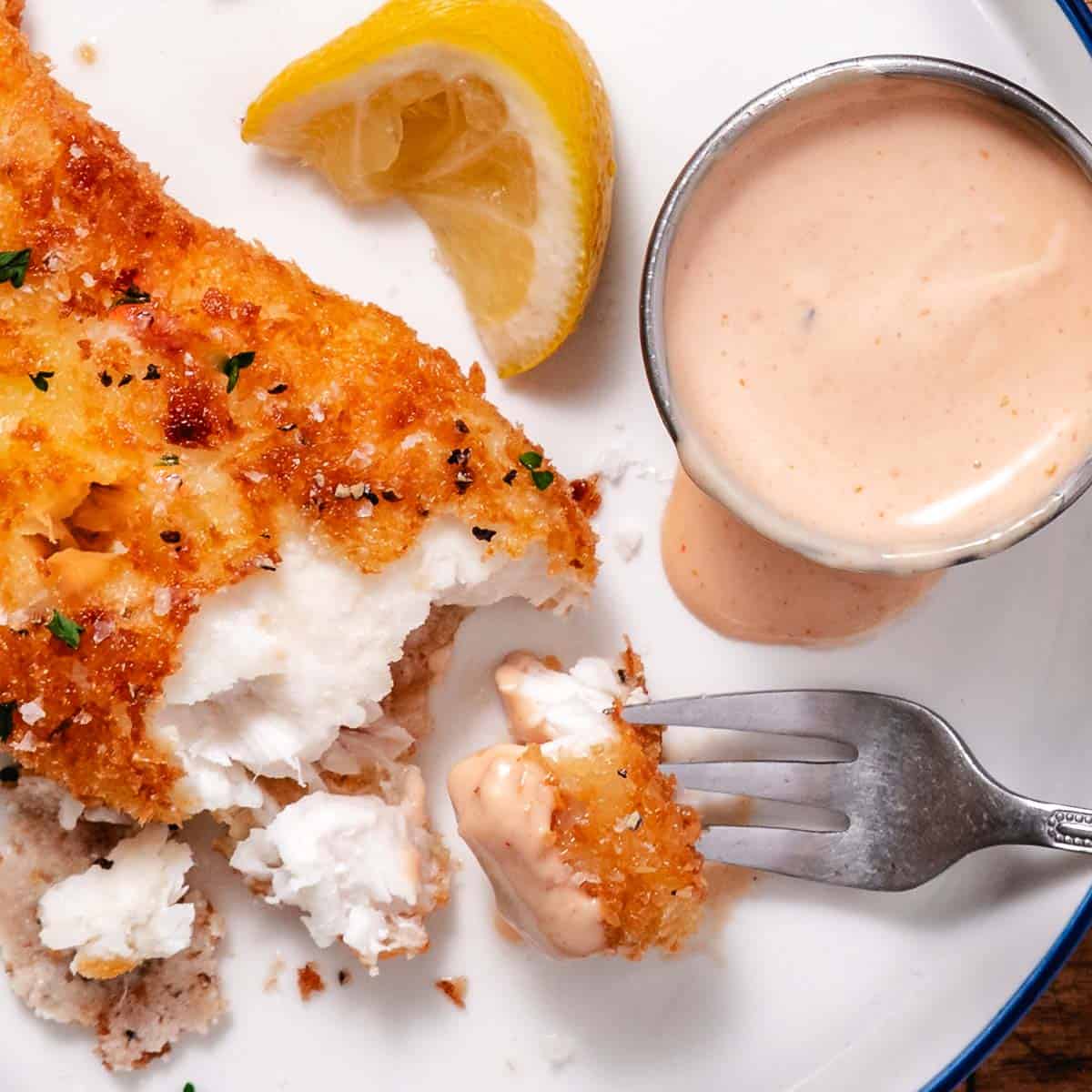Pan-fried halibut with pink sauce with a bite being lifted with a fork.