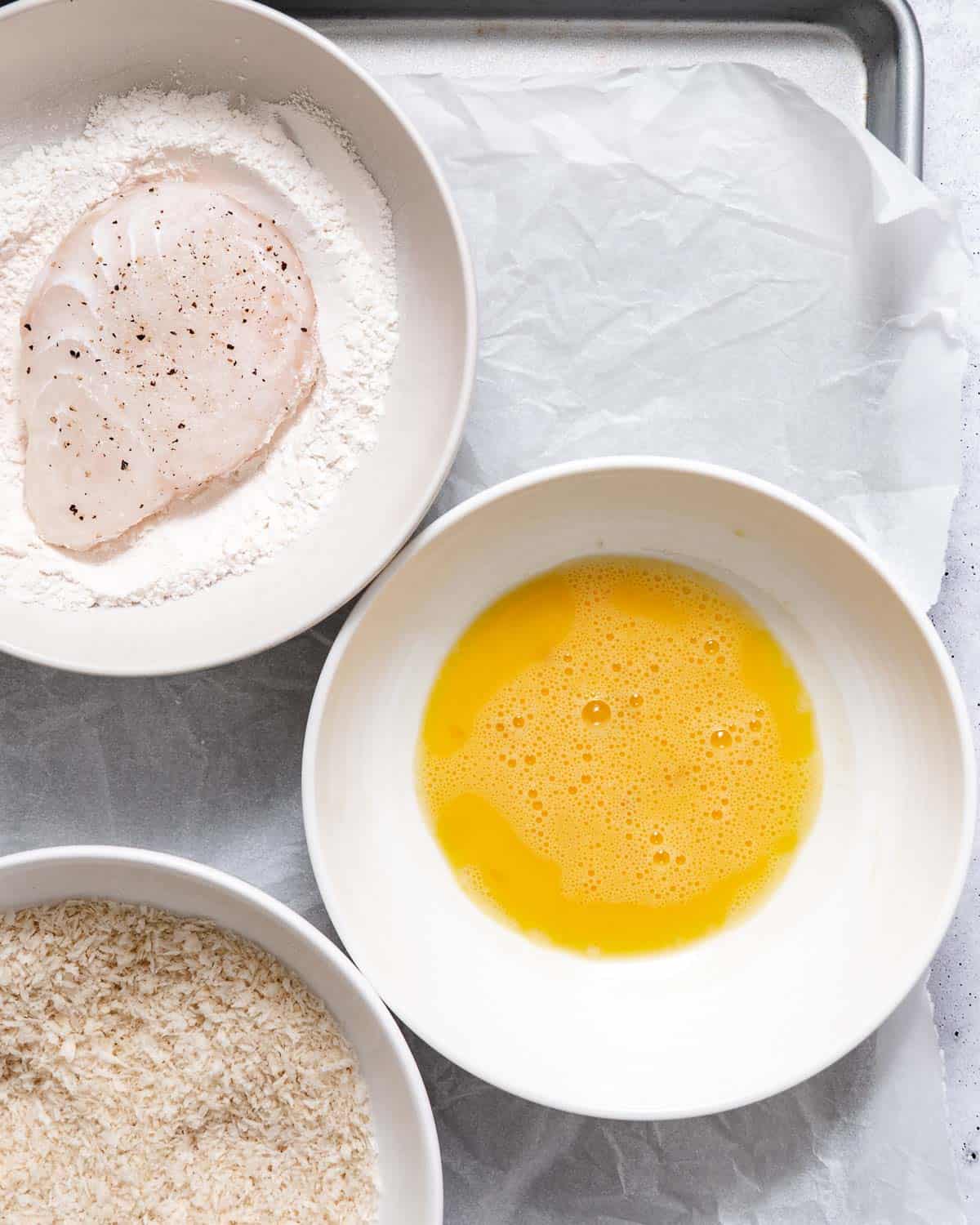 Breading stations for frying halibut. Flour, egg wash, and breadcrumbs in separate bowls.