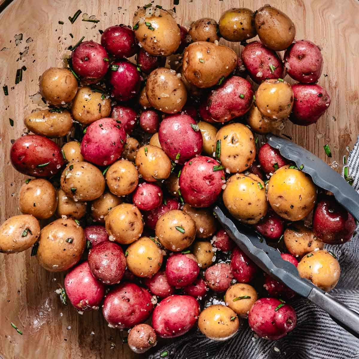 mixing red and yellow small potatoes in a mixing bowl with tongs