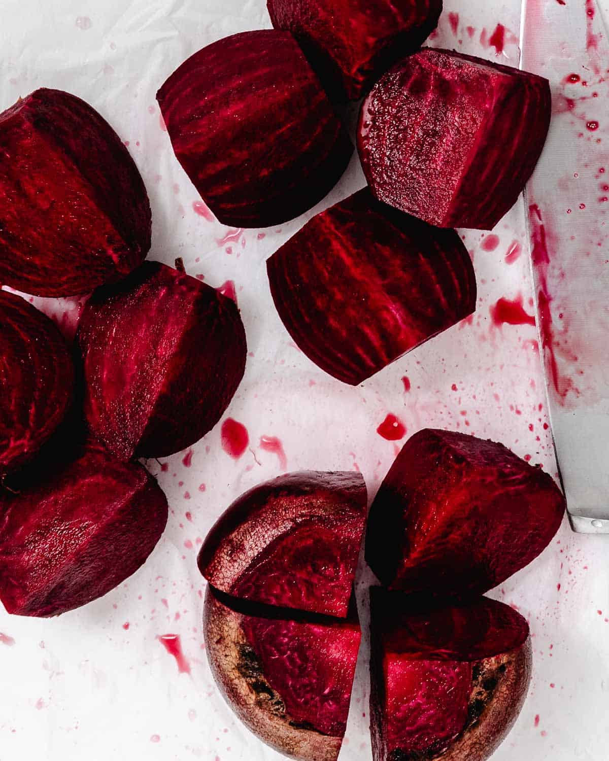 Peeled red beets cut into quarters on a parchment paper covered board.