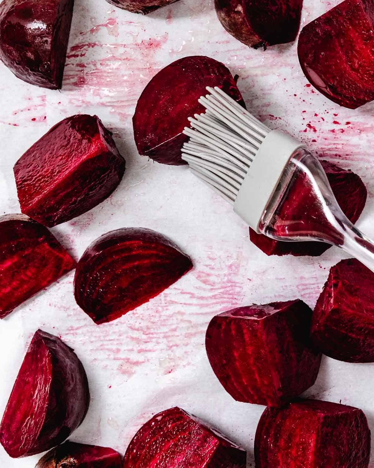 Raw red beets cut into pieces with a vegetable brush on a white surface, ready for cooking or roasting.