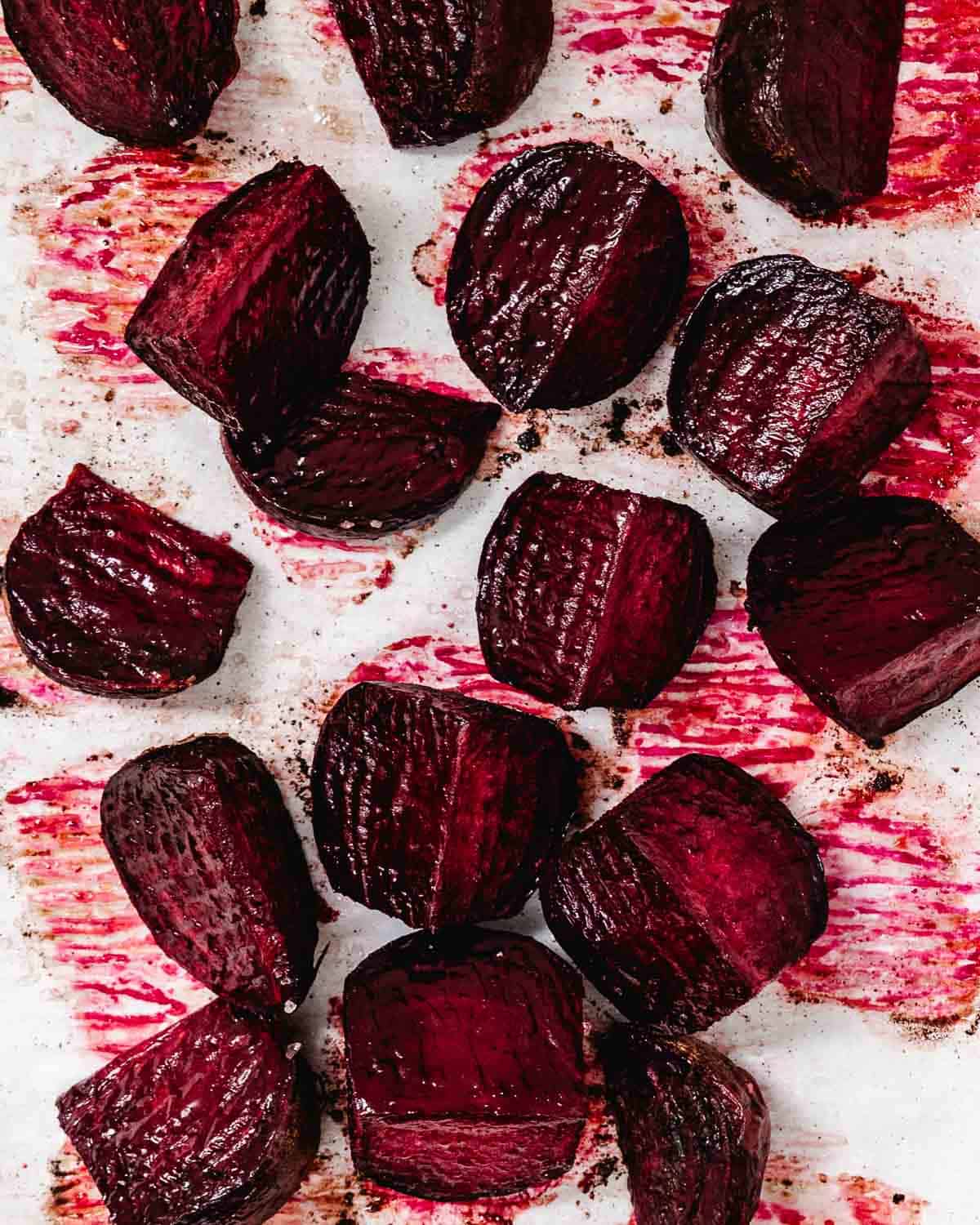 Roasted red beet quarters with browned edges on a parchment-lined sheet pan.