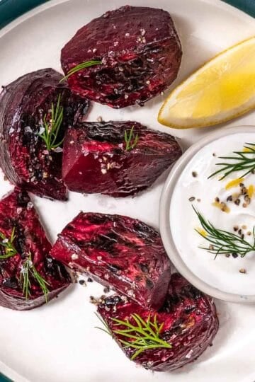 Roasted red beets on a white plate with dill yogurt sauce and a lemon wedge.
