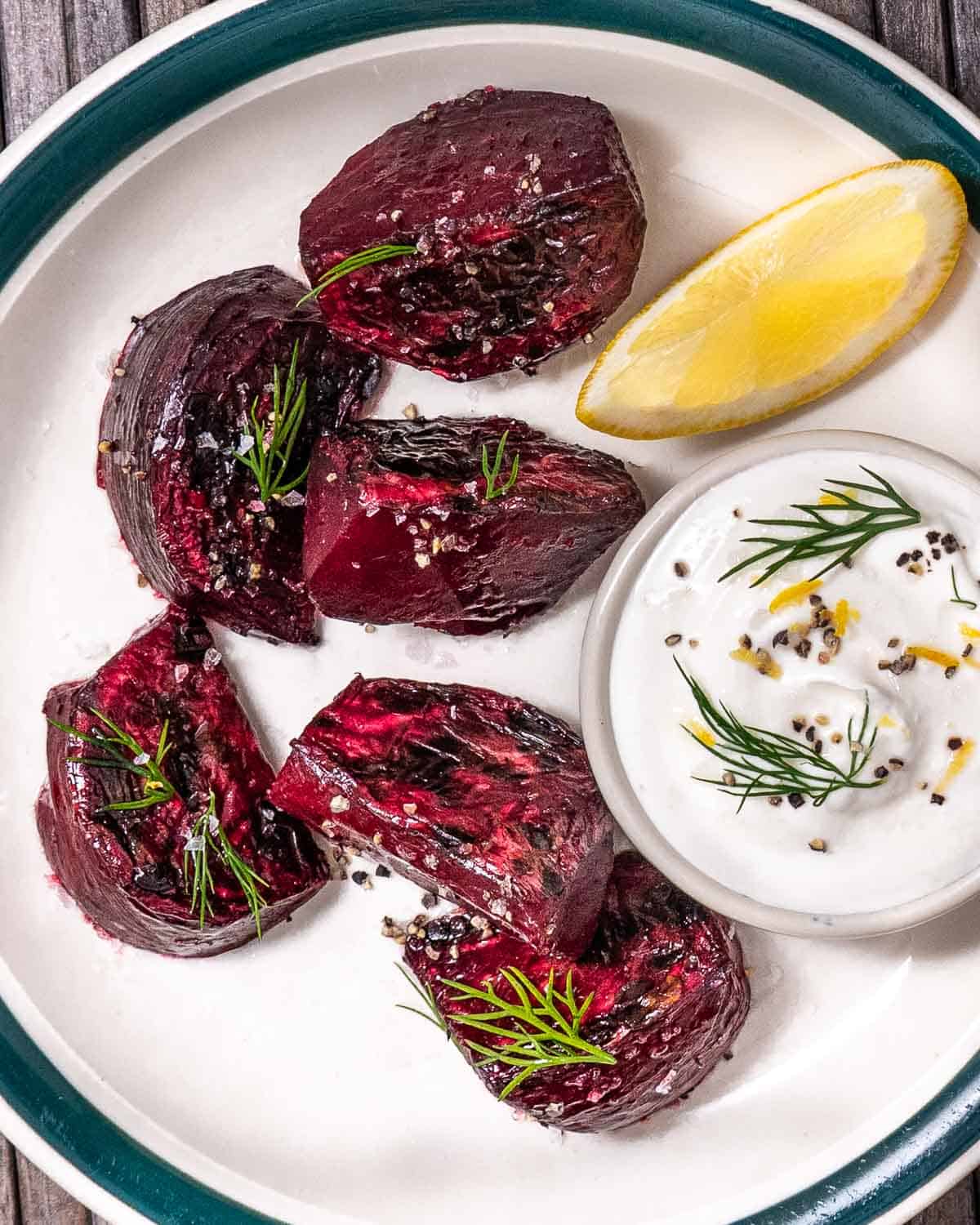 Roasted red beets on a white plate with sour cream sauce and a lemon wedge.