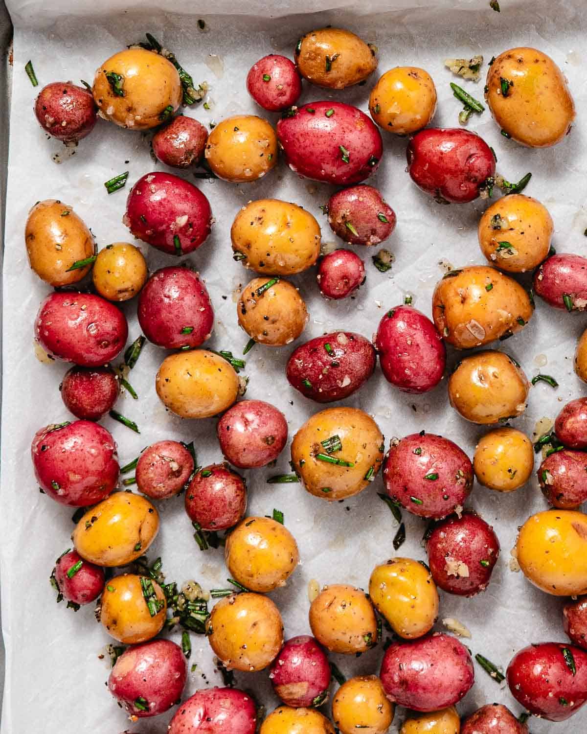 seasoned peewee potatoes with garlic and rosemary on a sheet pan before baking.