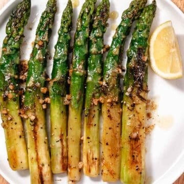 Thick asparagus with garlic-lemon butter and a fresh lemon wedge on a white platter.