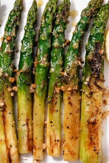 Thick asparagus with garlic-lemon butter and a fresh lemon wedge on a white platter.