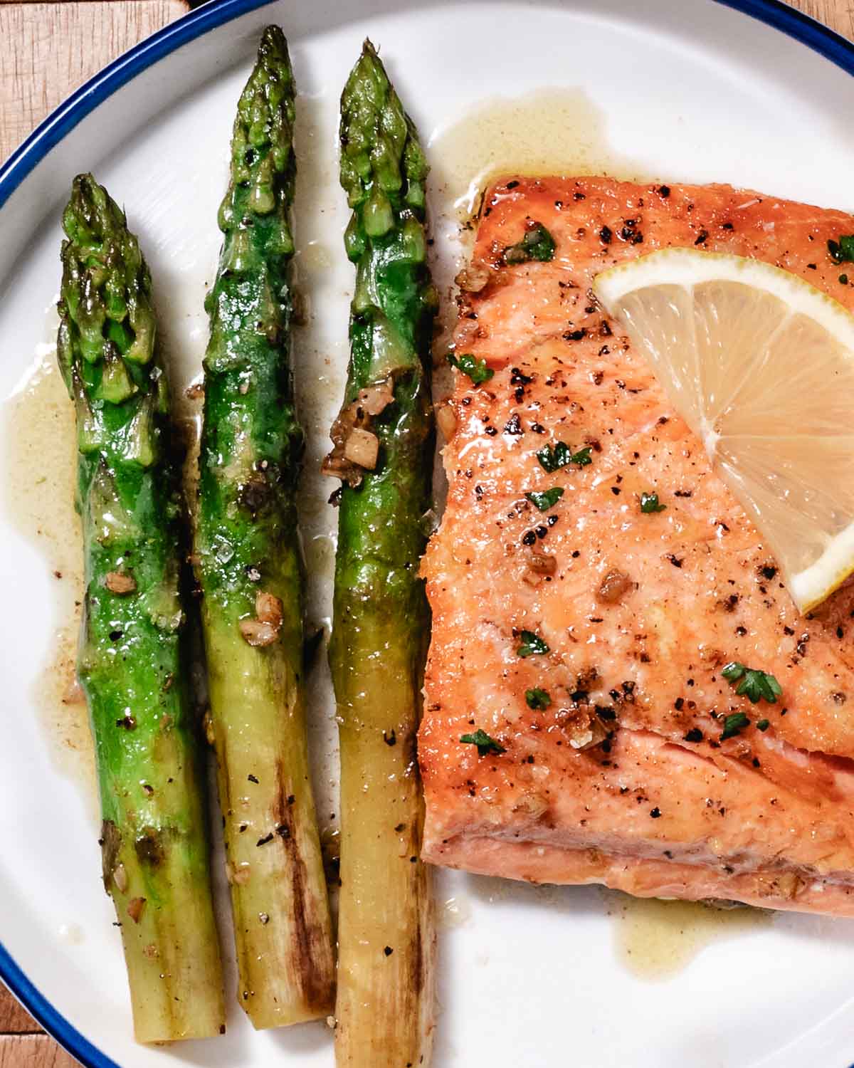 Pan-seared salmon with thick asparagus and lemon butter on a white plate.