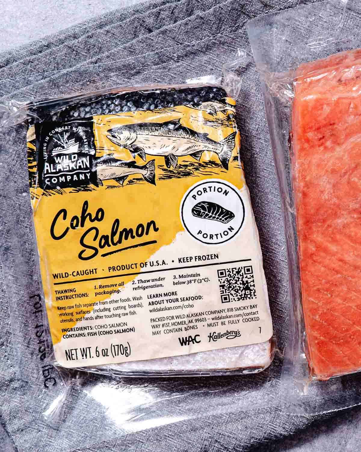 Frozen Wild Alaskan Company coho salmon portions in vacuum-sealed packaging on gray linen cloth.