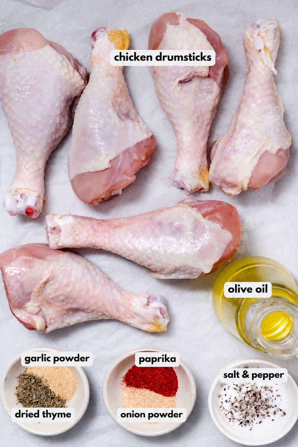 Ingredients for air fryer chicken drumsticks, including raw drumsticks, olive oil, thyme, paprika, garlic powder, onion powder, salt, and pepper.