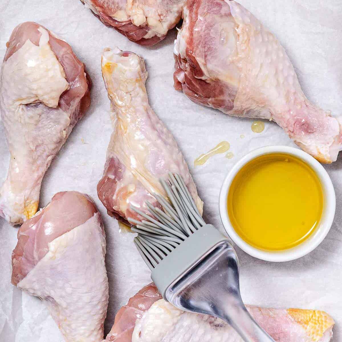 Brushing raw chicken drumsticks with olive oil before air frying.
