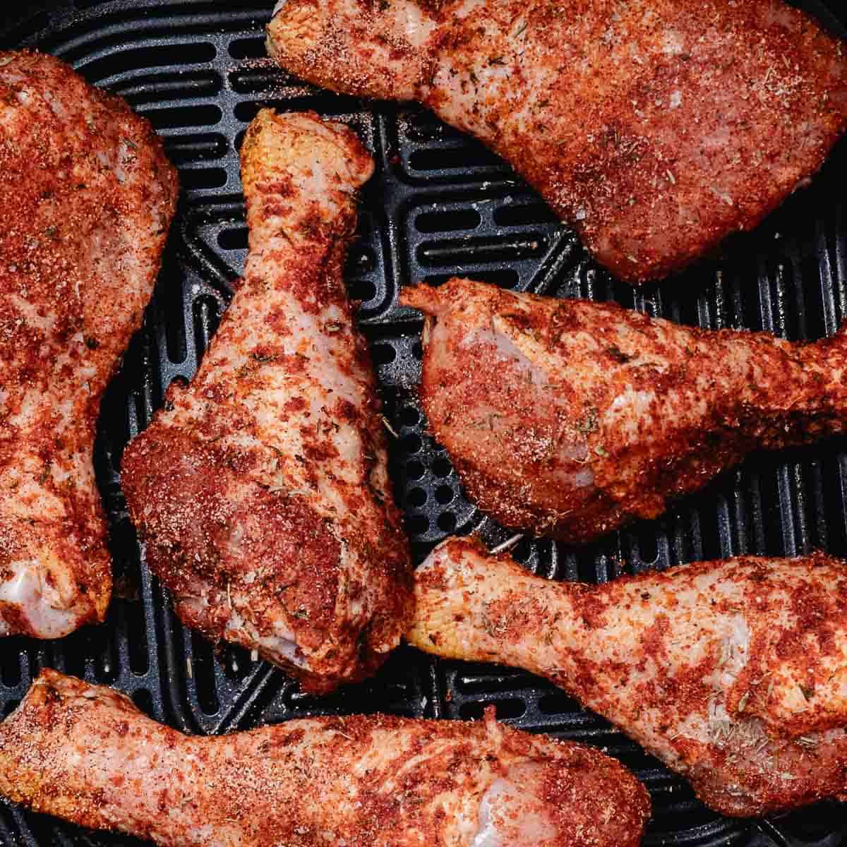 Seasoned chicken drumsticks arranged in a single layer in an air fryer basket.