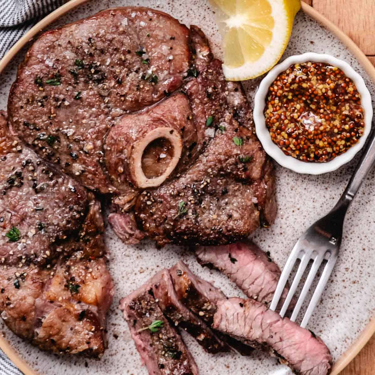 Air fryer lamb leg steak sliced and served with whole-grain mustard and a lemon wedge.