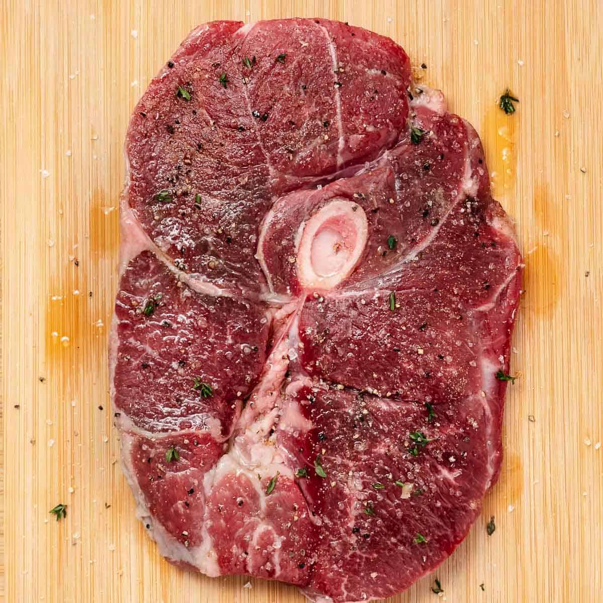 Raw bone-in lamb leg steak seasoned with olive oil, salt, pepper, and fresh thyme.