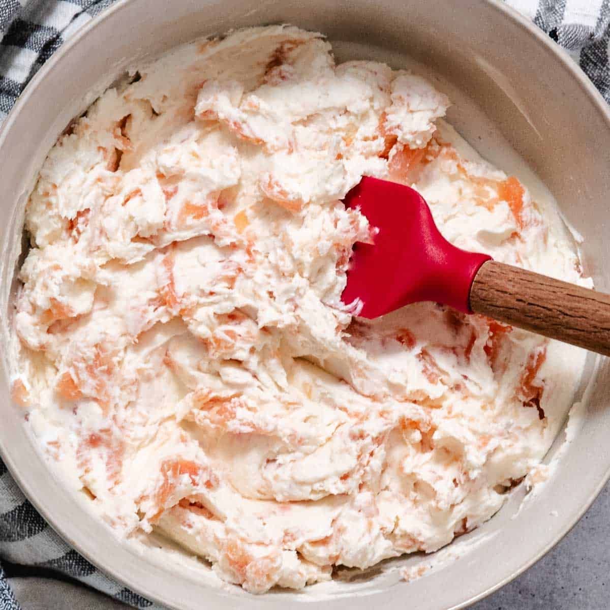 Smoked salmon cream cheese mixed together in a bowl with a red spatula.