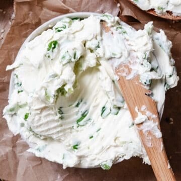 Bagel with scallion cream cheese spread and a knife.